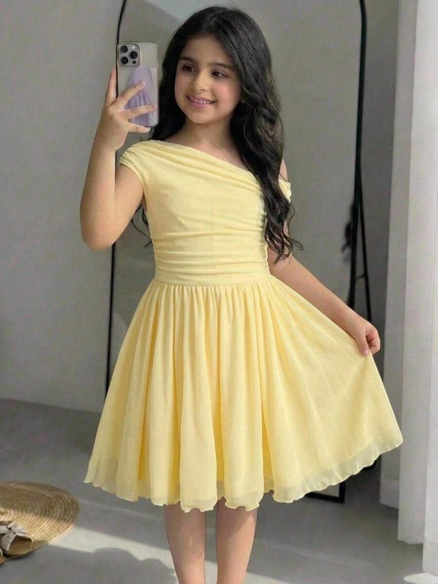 Tween girl wearing an apricot asymmetrical tiered sleeveless party dress with an A-line silhouette.
