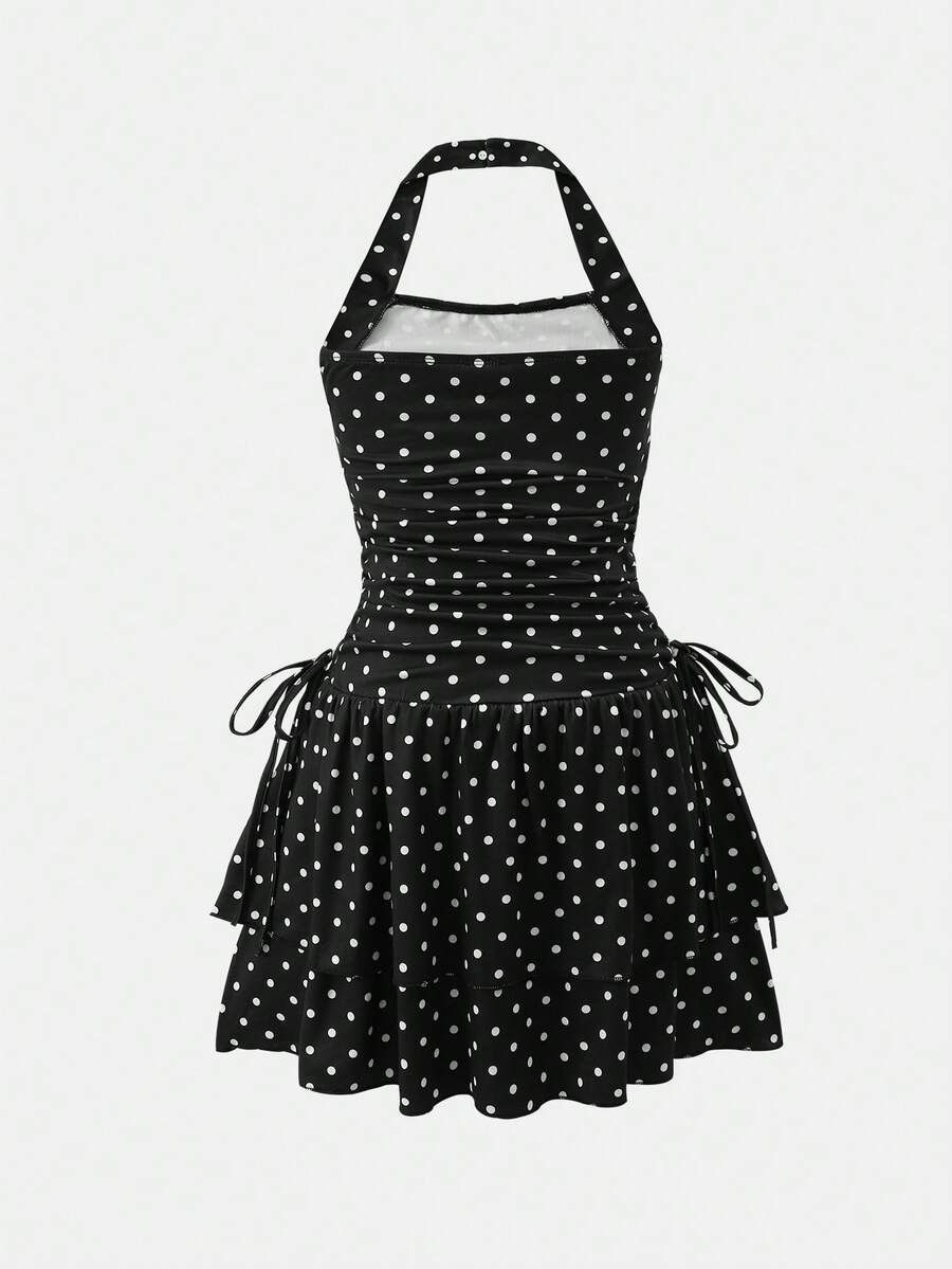 Tween girl wearing a black and white polka dot tiered cami dress with shoulder straps, a high waist, and a ruffle layered hem.