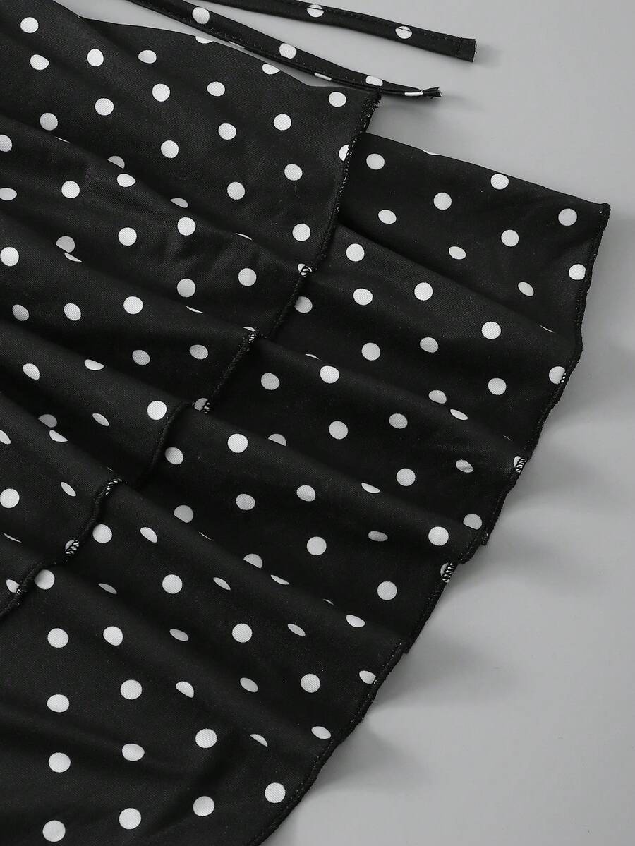 Tween girl wearing a black and white polka dot tiered cami dress with shoulder straps, a high waist, and a ruffle layered hem.