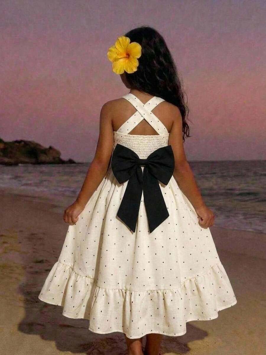 Pink sleeveless tween girls vacation dress with all-over fruit and vegetable print, strap neckline, belted high waist, cut-out detail, and flared ruffle hem.