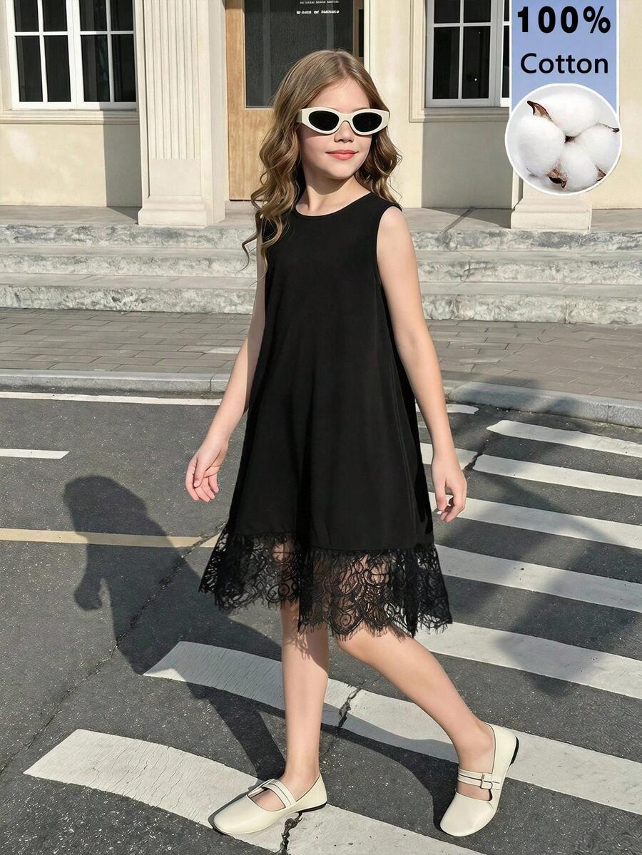 Tween girl wearing a sleeveless black tunic dress featuring a round neck, contrast lace details, and a straight hem.