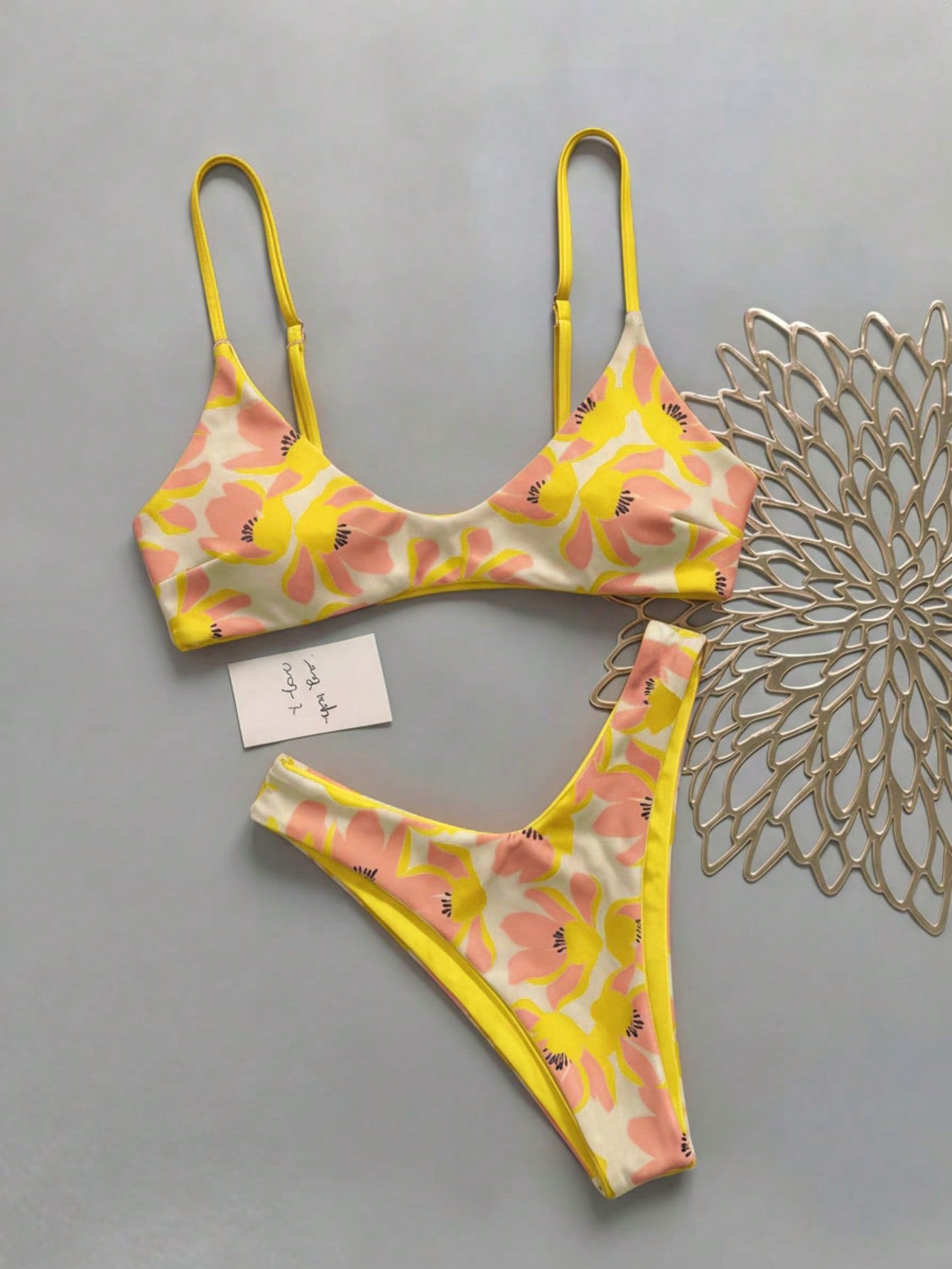 Women's pinkish orange floral print 2-piece bikini set featuring a backless wireless top with spaghetti straps and matching mid-waist bikini bottoms.