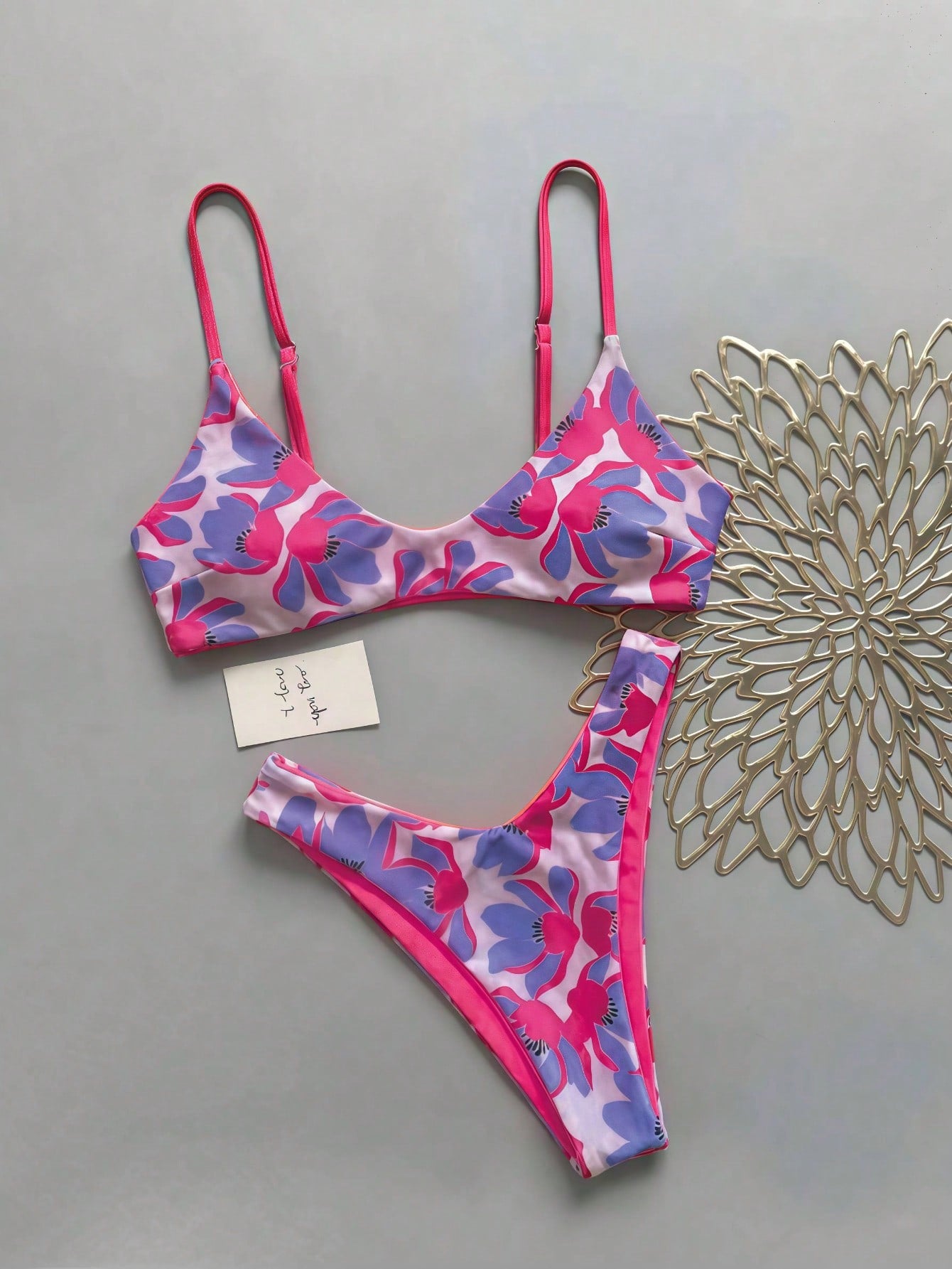 Women's pinkish orange floral print 2-piece bikini set featuring a backless wireless top with spaghetti straps and matching mid-waist bikini bottoms.