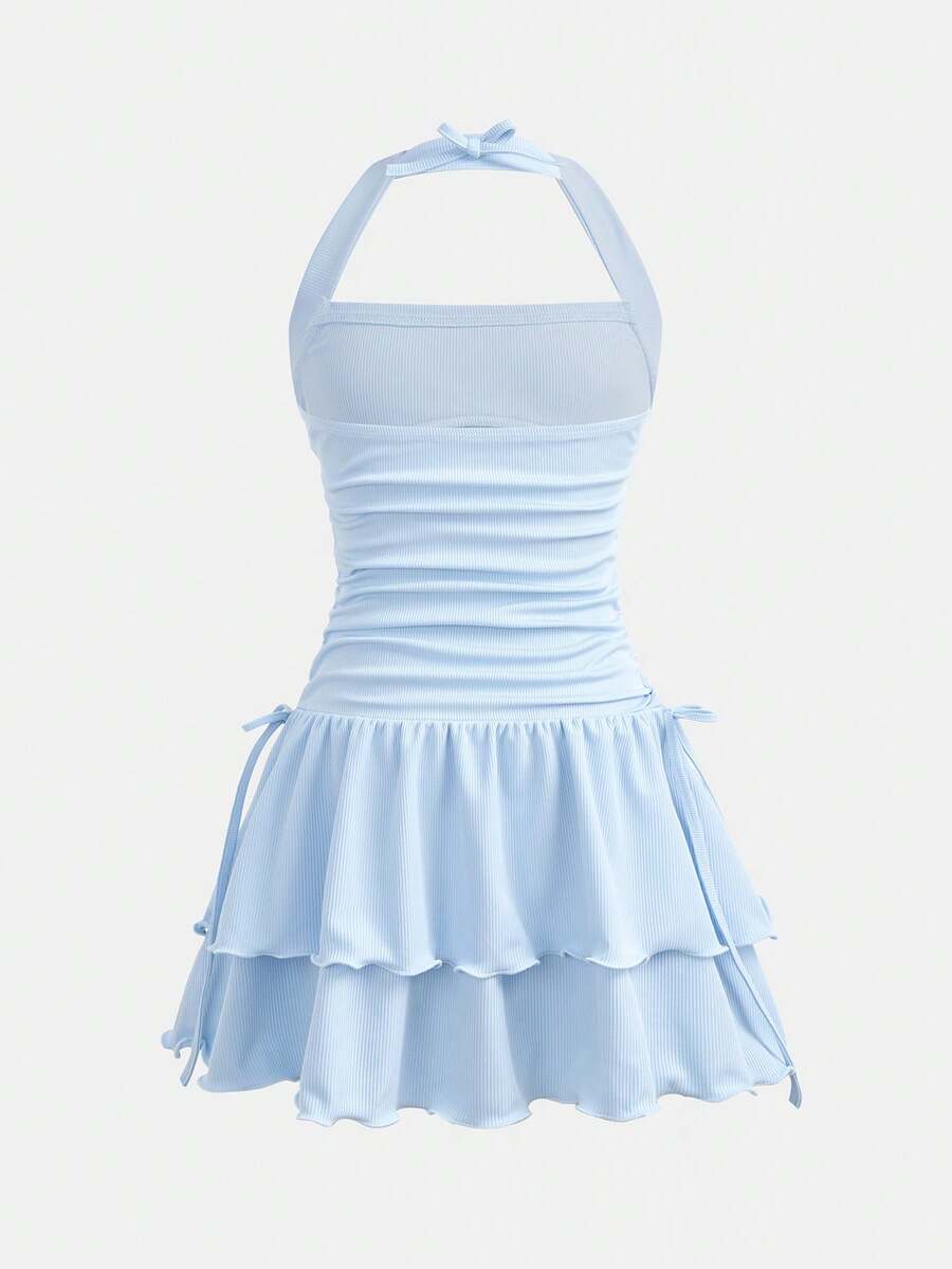 Tween girl wearing a black and white polka dot tiered cami dress with shoulder straps, a high waist, and a ruffle layered hem.