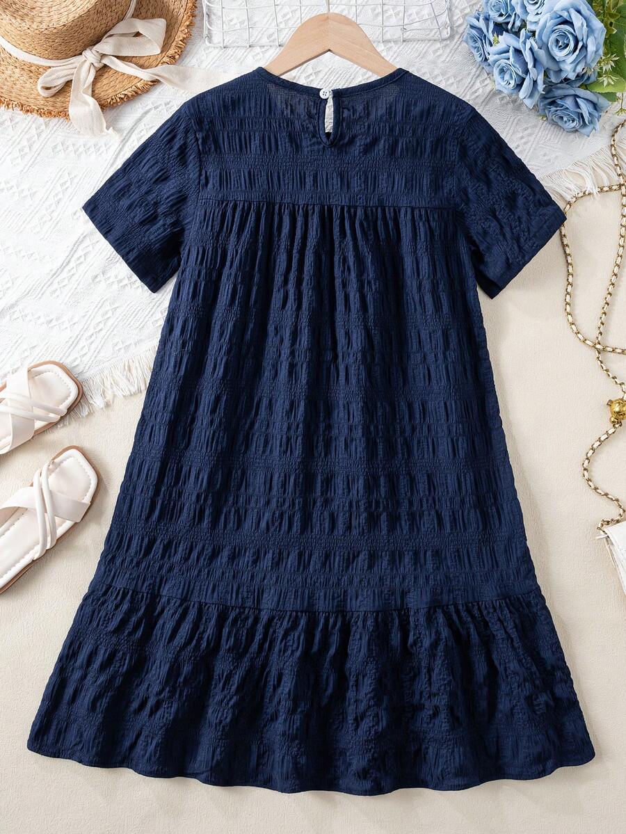 Tween girl wearing an Army Green textured short sleeve smock midi dress with round neck and ruffle flounce hem.
