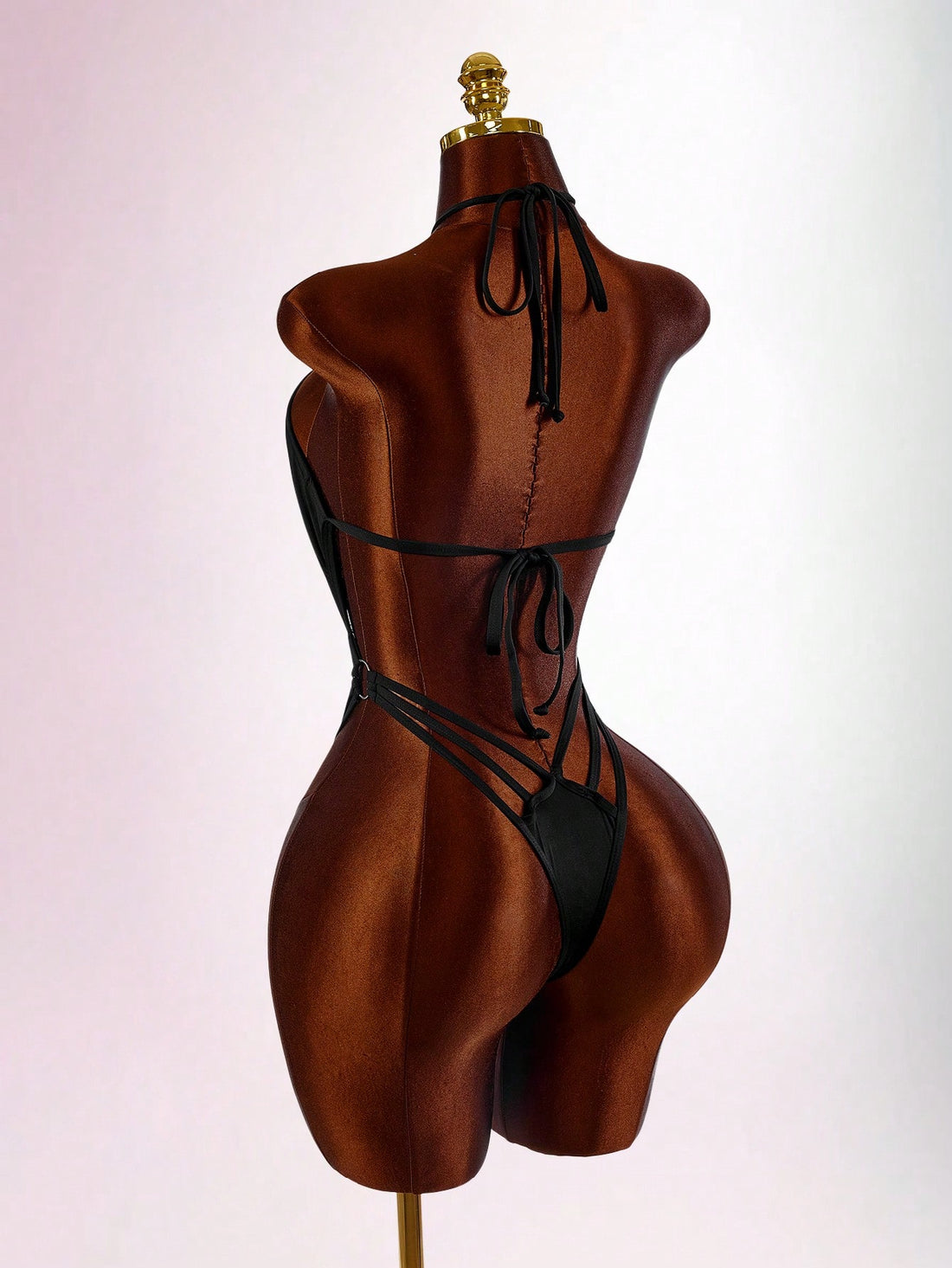 Women's black criss-cross halter backless one-piece swimsuit featuring strappy tie-up details, waist cutouts, and a high cut thong bottom.