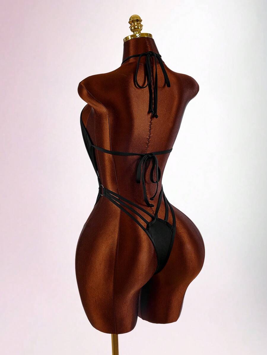 Women's black criss-cross halter backless one-piece swimsuit featuring strappy tie-up details, waist cutouts, and a high cut thong bottom.
