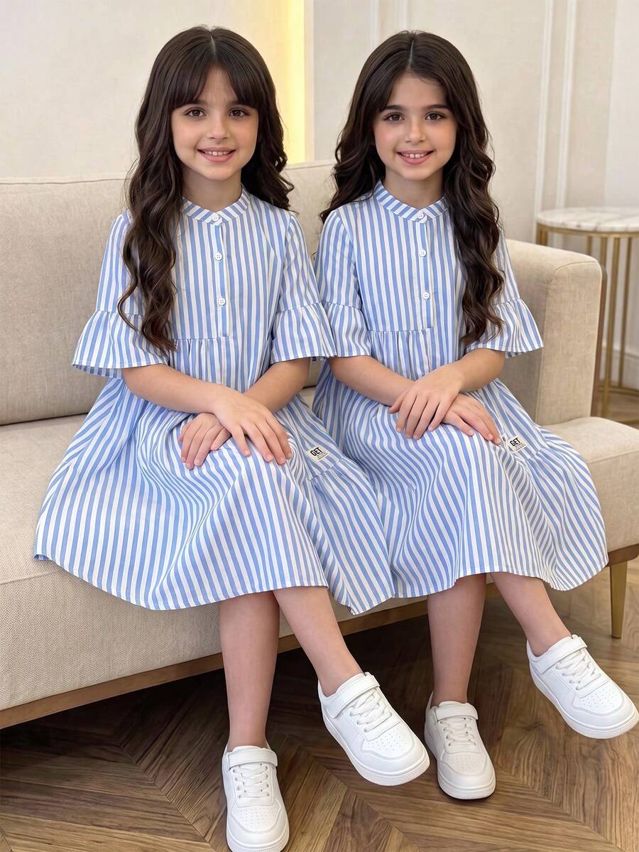 Tween girl wearing a black striped smock shirt dress with flounce half sleeves, a stand collar, and a ruffled hem.