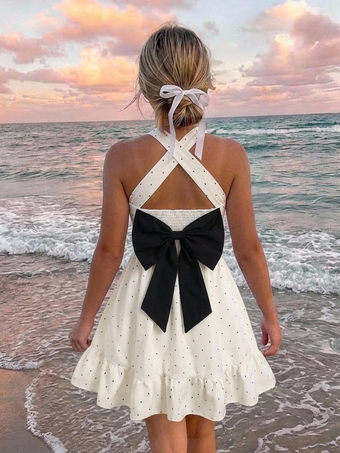 Pink sleeveless tween girls vacation dress with all-over fruit and vegetable print, strap neckline, belted high waist, cut-out detail, and flared ruffle hem.