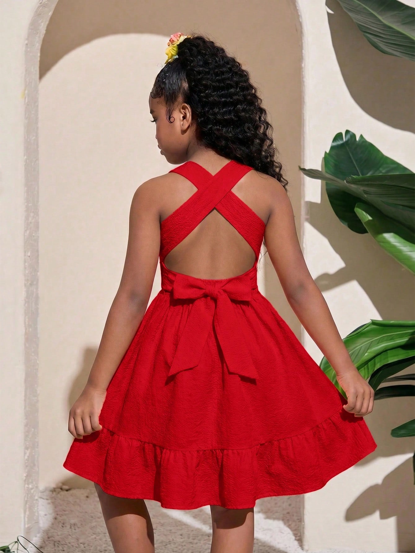 Pink sleeveless tween girls vacation dress with all-over fruit and vegetable print, strap neckline, belted high waist, cut-out detail, and flared ruffle hem.