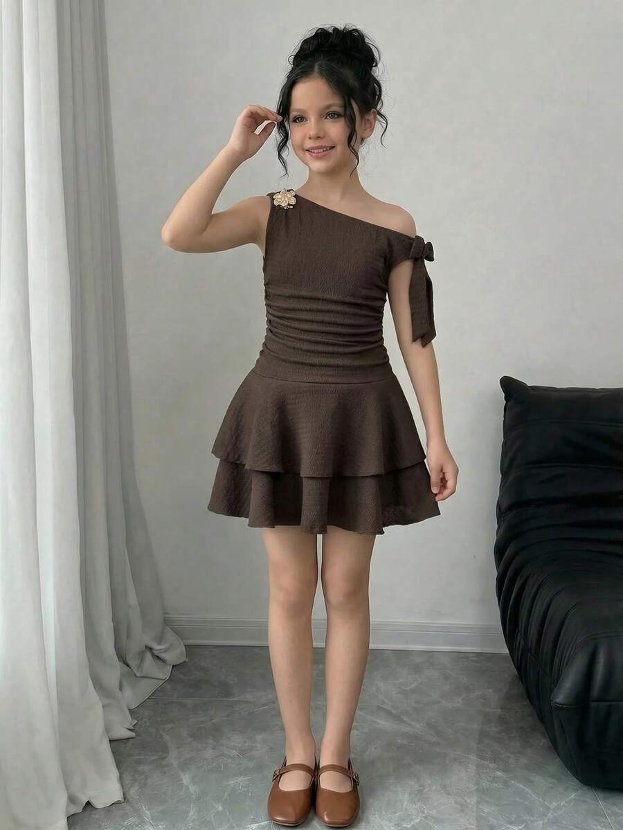 Tween girl wearing an apricot asymmetric skater dress with ruffle and applique details for party and formal occasions.
