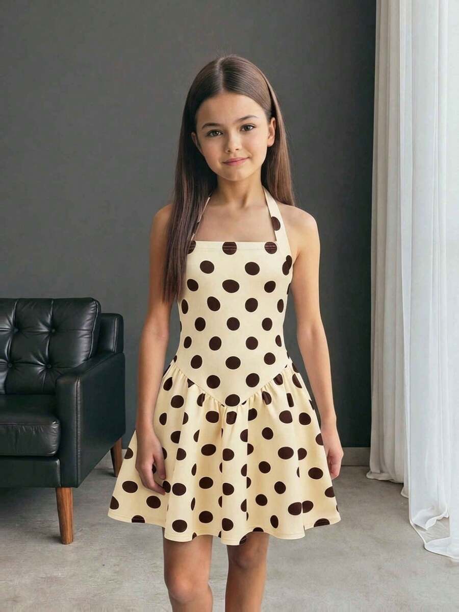 Tween girl wearing a black and white polka dot tiered cami dress with shoulder straps, a high waist, and a ruffle layered hem.