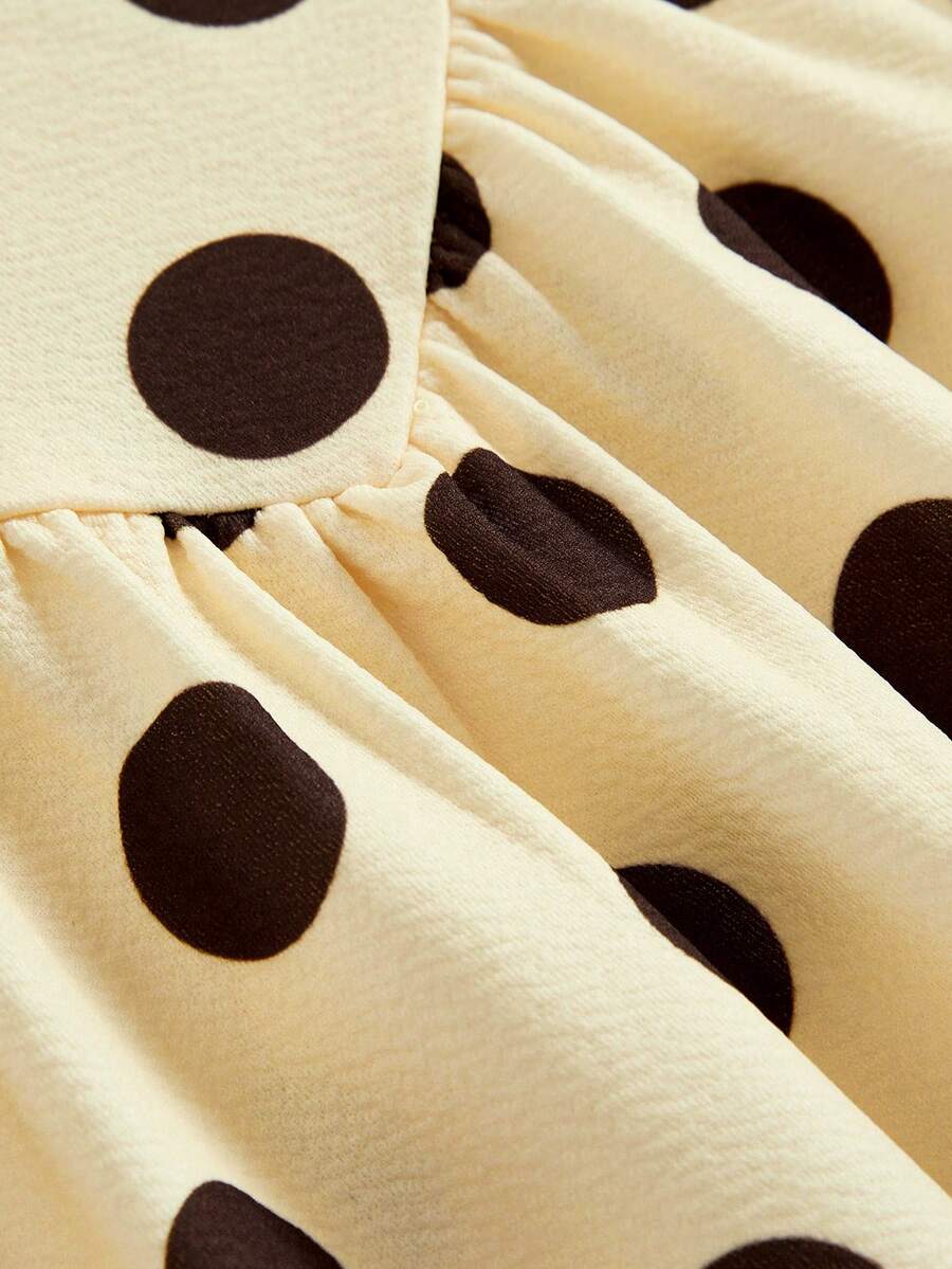Tween girl wearing a black and white polka dot tiered cami dress with shoulder straps, a high waist, and a ruffle layered hem.