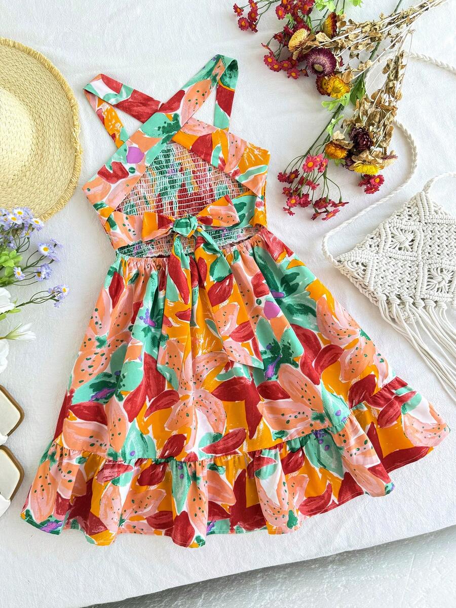 Pink sleeveless tween girls vacation dress with all-over fruit and vegetable print, strap neckline, belted high waist, cut-out detail, and flared ruffle hem.