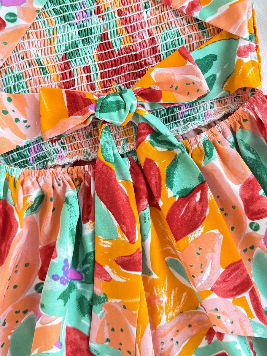 Pink sleeveless tween girls vacation dress with all-over fruit and vegetable print, strap neckline, belted high waist, cut-out detail, and flared ruffle hem.