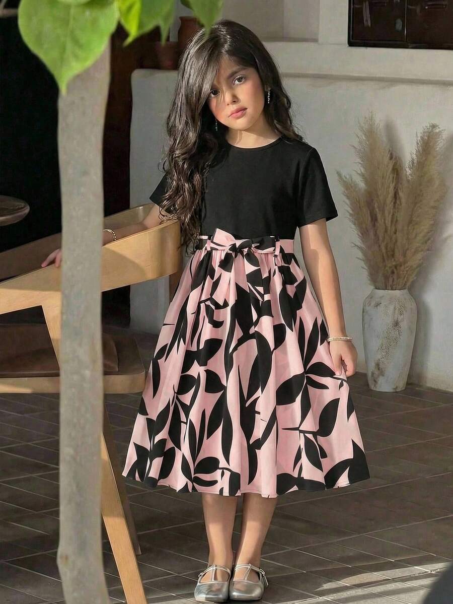 Tween girl wearing an apricot short sleeve A-line dress featuring a round neck, high waist with a belt, and flared hem.