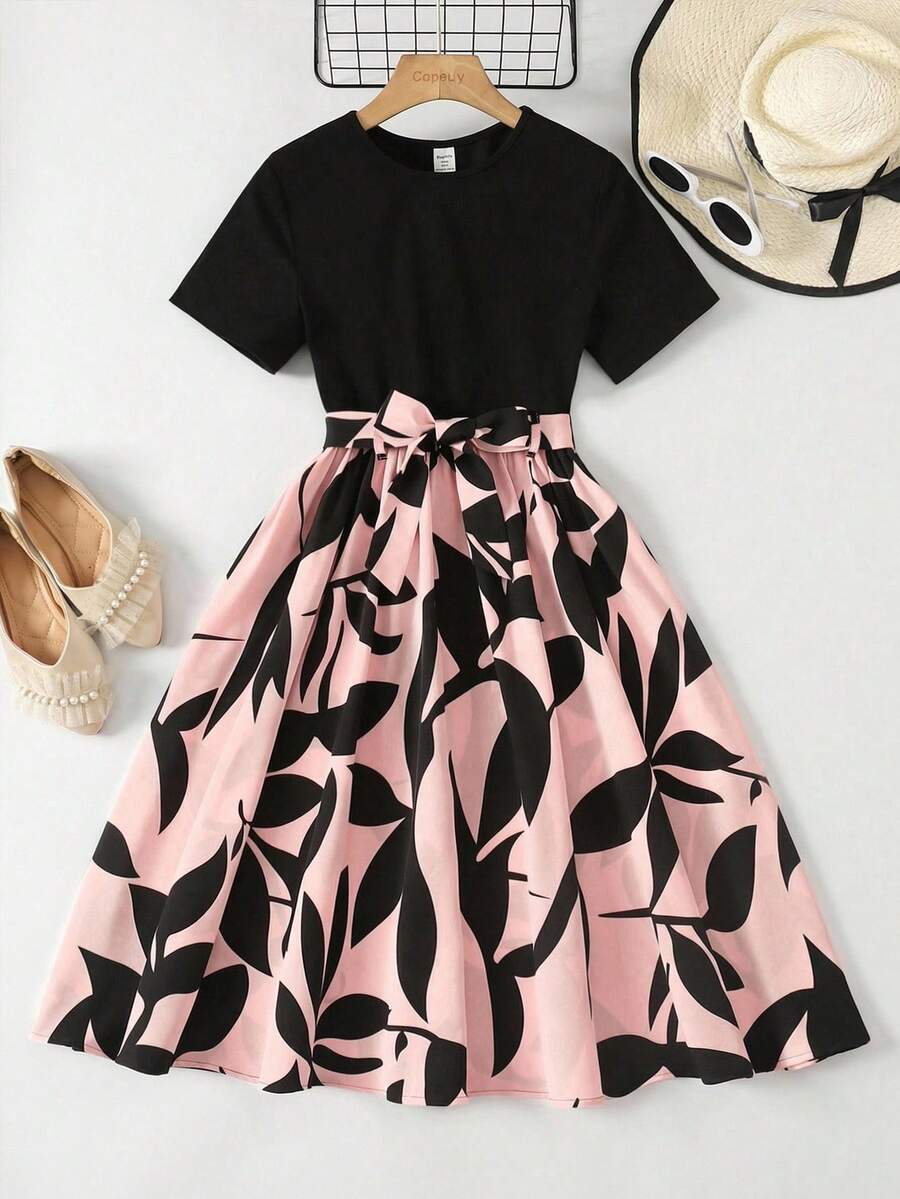 Tween girl wearing an apricot short sleeve A-line dress featuring a round neck, high waist with a belt, and flared hem.