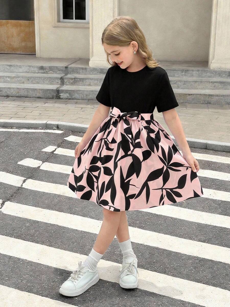 Tween girl wearing an apricot short sleeve A-line dress featuring a round neck, high waist with a belt, and flared hem.