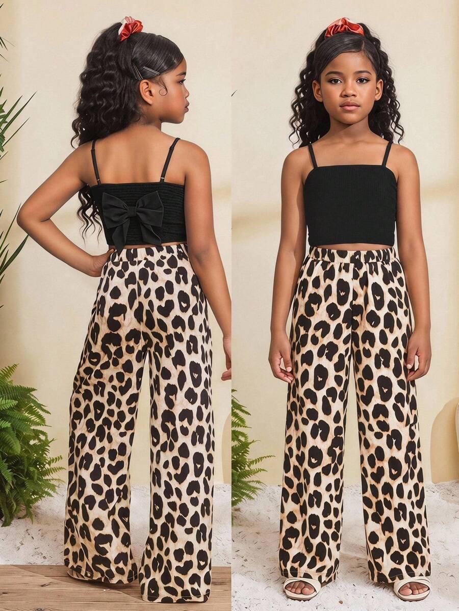 Tween girl wearing a black sleeveless spaghetti strap camisole top with 3D bow decor and matching leopard print wide leg long pants.