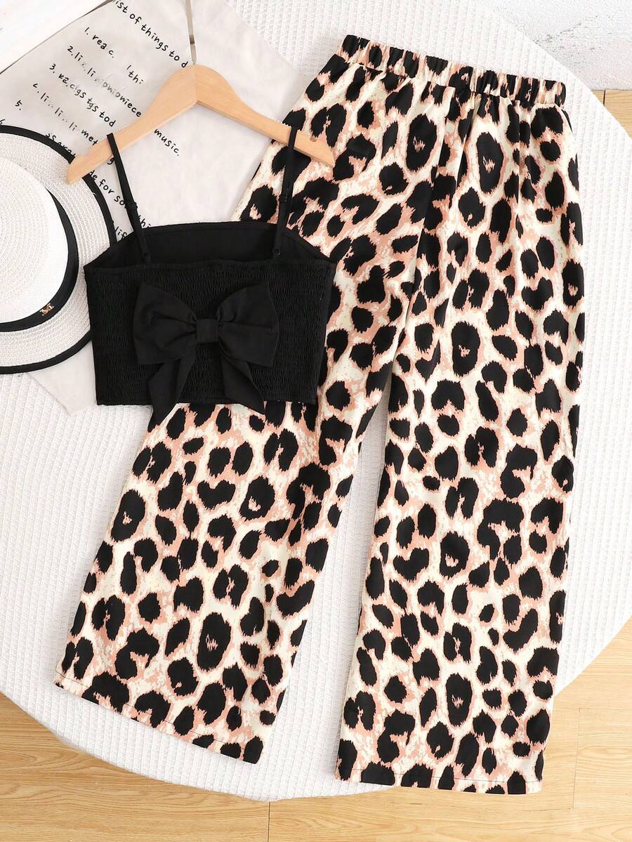 Tween girl wearing a black sleeveless spaghetti strap camisole top with 3D bow decor and matching leopard print wide leg long pants.
