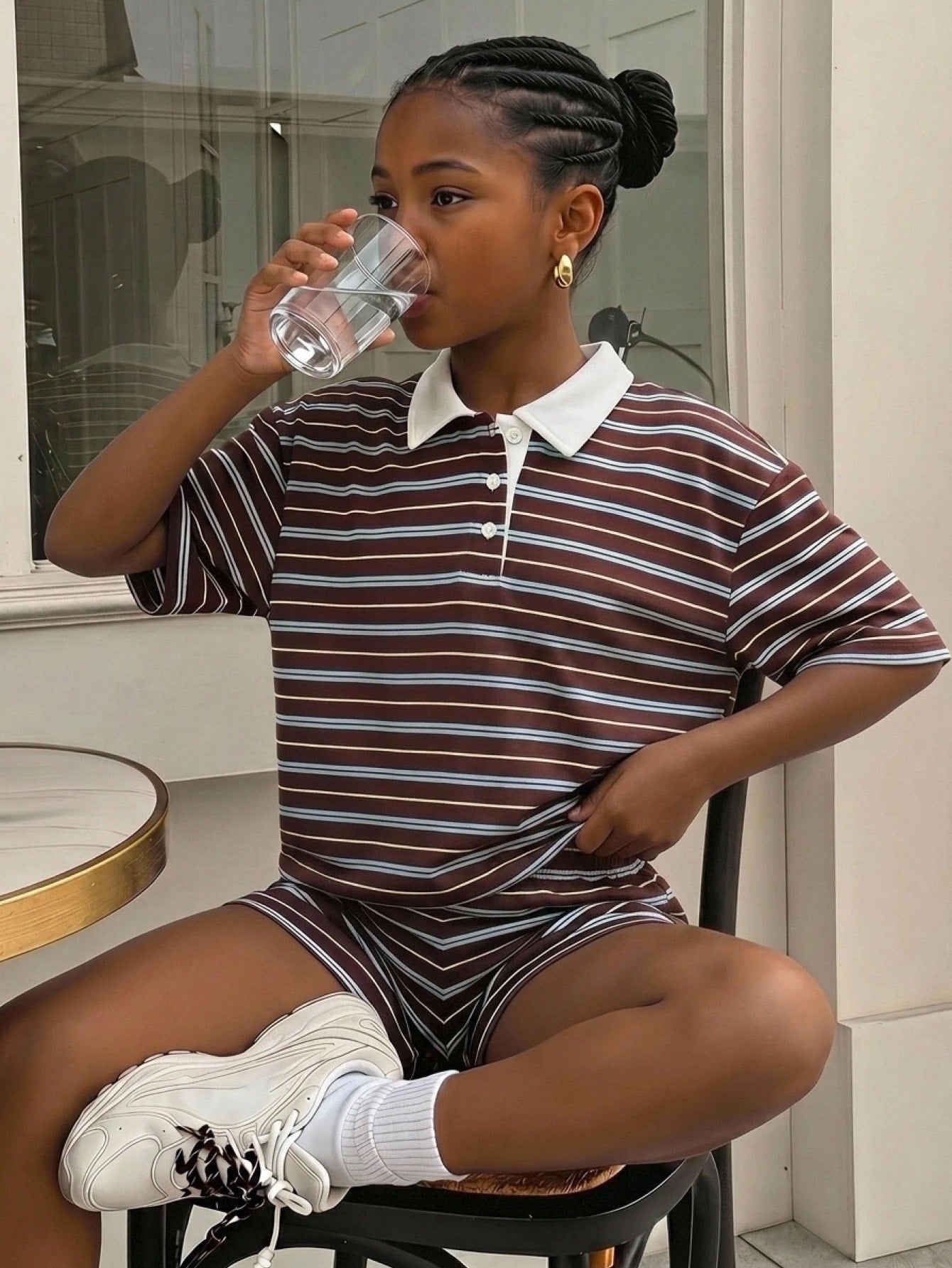 Tween girl wearing a black and white striped drop-shoulder crew neck t-shirt with bow embroidery paired with matching tie-waist shorts.